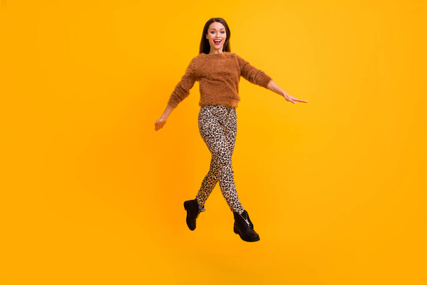 Full length photo of pretty funky lady jumping up high youth trend look walk low prices shopping center wear fluffy pullover leopard pants shoes isolated yellow color background - Foto, imagen