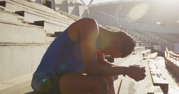 Oldalnézet egy vegyes verseny férfi sportoló egy üres sportstadionban, ül és koncentrál a verseny előtt, lassított felvétel - Felvétel, videó