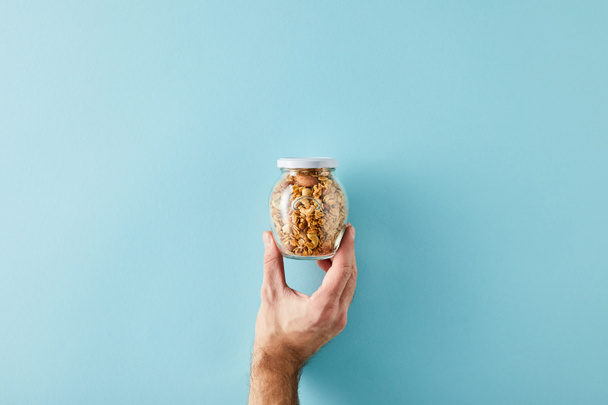 Καλλιεργημένη άποψη του ανθρώπου κρατώντας βάζο από granola σε μπλε φόντο - Φωτογραφία, εικόνα