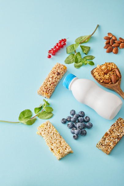 Bottle of yogurt, berries, cereal bars, mint and almonds on blue background - Photo, Image