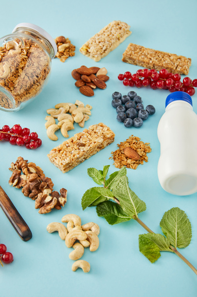 Bottle of yogurt, berries, mint, jar of granola and nuts on blue background - Φωτογραφία, εικόνα