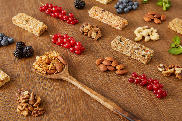 Berries, nuts, cereal bars and spatula with granola on wooden background - Valokuva, kuva