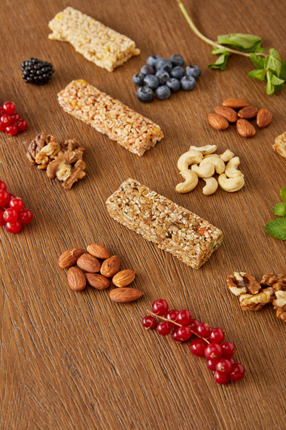 Selective focus of berries, nuts, cereal bars, mint on wooden background - Fotoğraf, Görsel