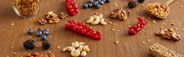Blueberries, redcurrants, walnuts, almonds, cashews, cereal bar on wooden background, panoramic shot - Photo, Image