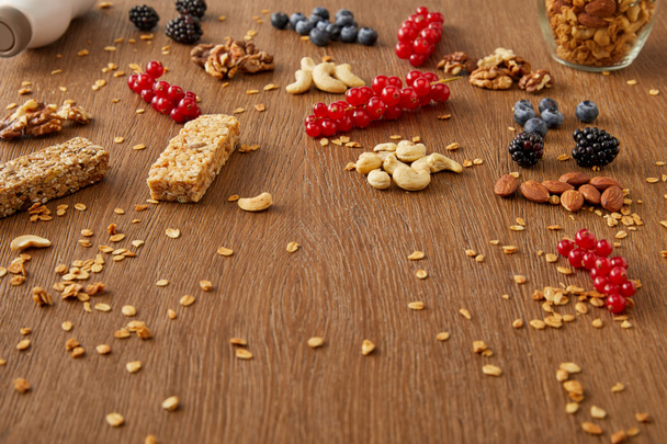 Redcurrants, blueberries, walnuts, almonds, cashews, oat flakes and cereal bars on wooden background - Foto, afbeelding