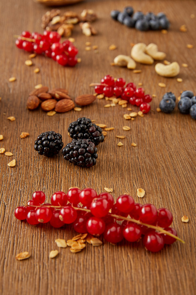 Enfoque selectivo de grosellas rojas, arándanos, copos de avena y frutos secos sobre fondo de madera
 - Foto, Imagen