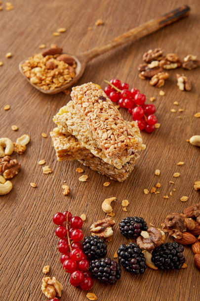 Селективный фокус зерновых батончиков, лопаток с мюсли, красной смородины, ежевики и орехов на деревянном фоне
 - Фото, изображение