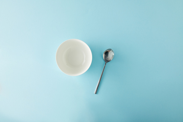 Top view of empty bowl and teaspoon on blue background - Zdjęcie, obraz