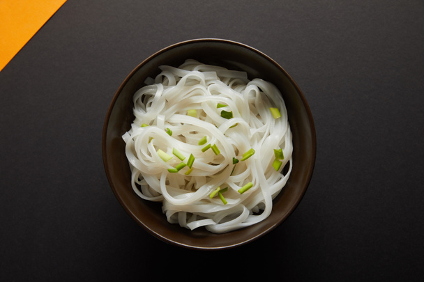 top view of rice noodles in bowl on yellow and black surface - Photo, Image