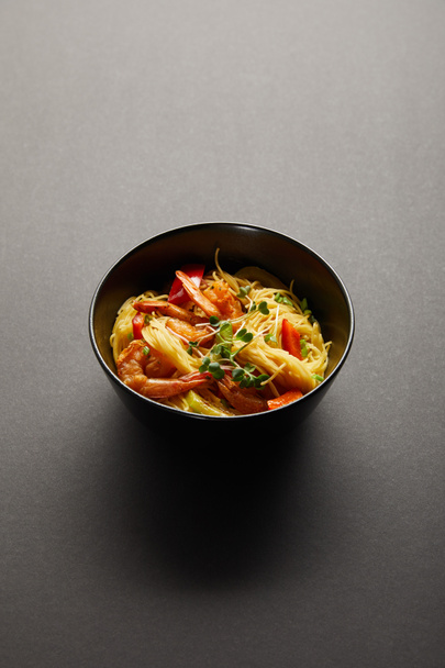 macarrão com camarões e legumes em tigela sobre fundo preto
 - Foto, Imagem