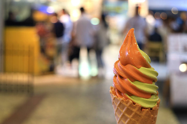 Melkthee en groene thee Tweekleurige Soft Serve Ice Cream Cone, wazig winkelcentrum op de achtergrond - Foto, afbeelding