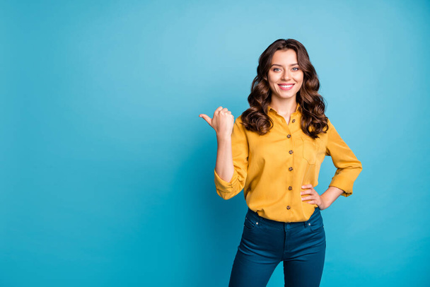 Kuva ihana liiketoiminnan johtaja nainen osoittaa peukalo sormi tyhjä tila neuvoo uusi tuote edulliseen hintaan kulumista keltainen paita housut eristetty sininen väri tausta
 - Valokuva, kuva