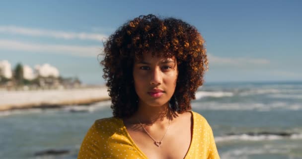 Portrait of mixed race woman enjoying time by the seaside on a sunny day with blue sky, looking at camera, slow motion - Кадри, відео