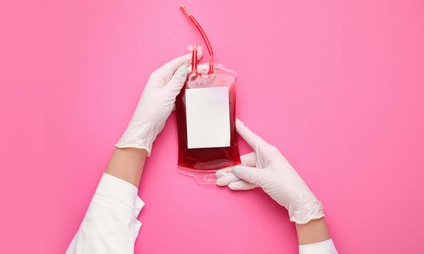 Manos del médico con paquete de sangre para transfusión sobre fondo de color
 - Foto, Imagen