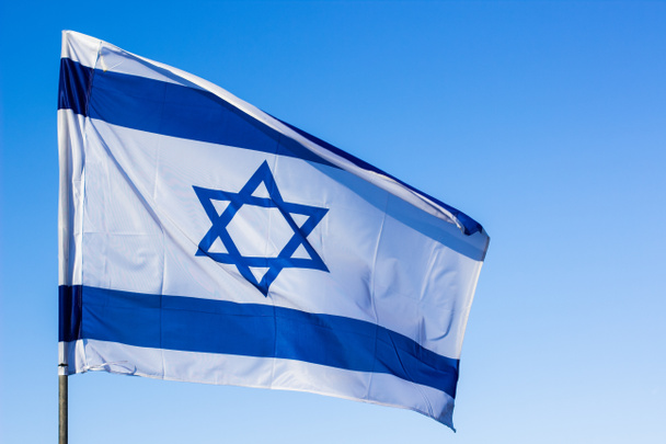 Israeli flag blue and white color with star of David national symbol fluttering on a wind on sky background - Foto, imagen
