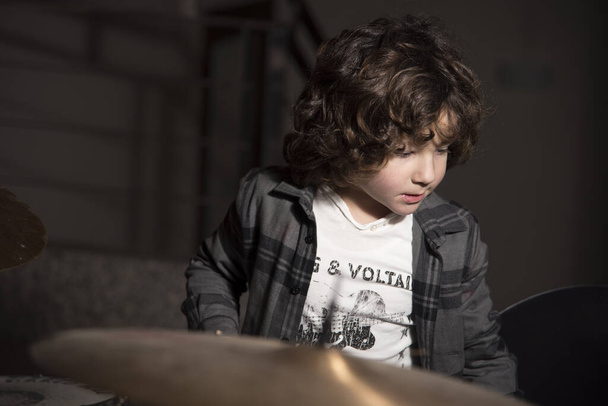 Curly-haired boy and gray shirt of shirtmakers playing drums like a pro. Fun and passion playing music - Foto, Bild