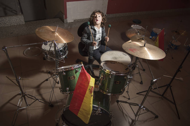 Curly-haired boy and gray shirt of shirtmakers playing drums like a pro. Fun and passion playing music - Fotoğraf, Görsel