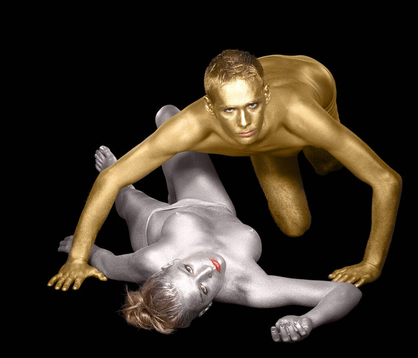 studio shot of a silver bodypainted woman and man in golden dark back - Photo, image