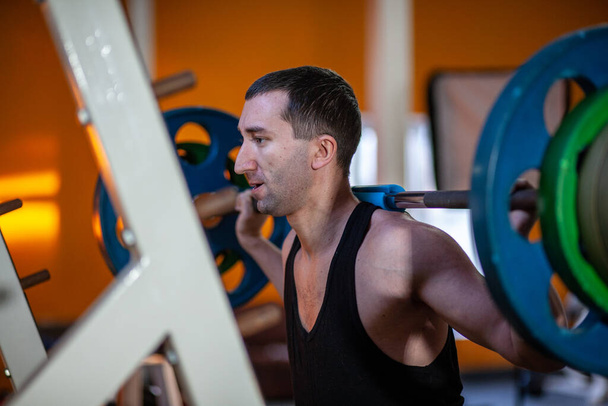 Hombre en el gimnasio levanta la barra, entrenamiento muscular con pesas, levantamiento de pesas
. - Foto, imagen