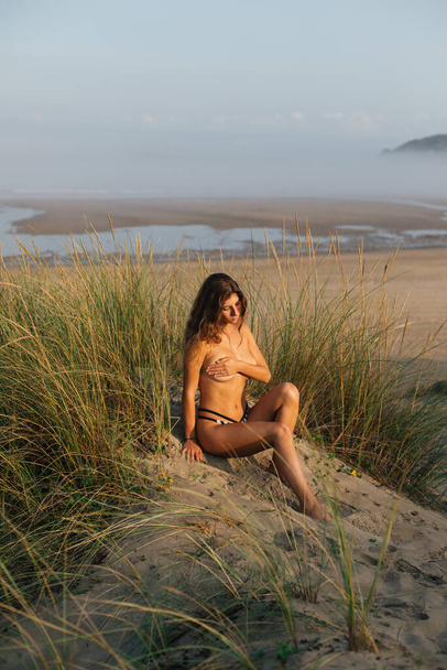 Natural beautiful woman tanning and relaxing in topless at the beach in the morning. Playa de Salinas, Asturias, Spain. - Photo, image
