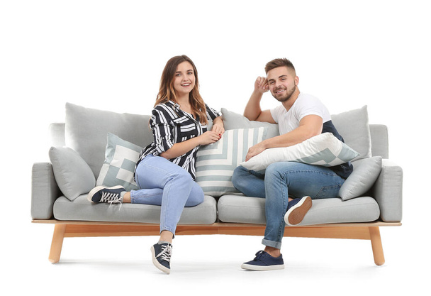 Nuori pari istuu sohvalla valkoista taustaa vasten
 - Valokuva, kuva