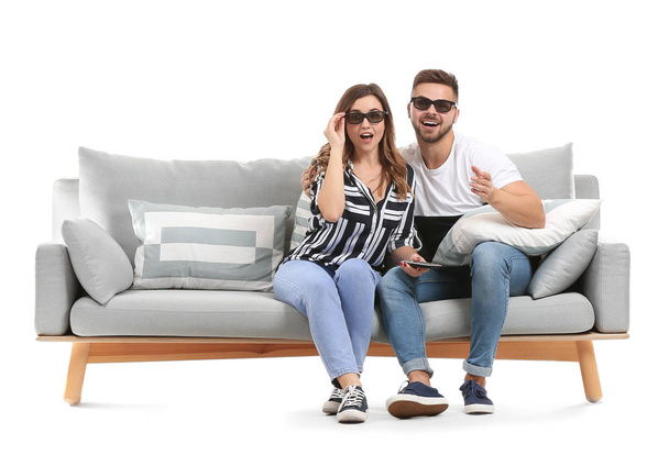 Young couple watching TV while sitting on sofa against white background - Photo, Image