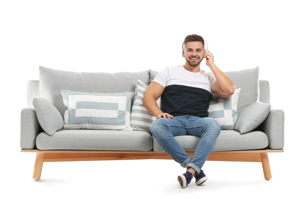 Young man listening to music while sitting on sofa against white background - Zdjęcie, obraz