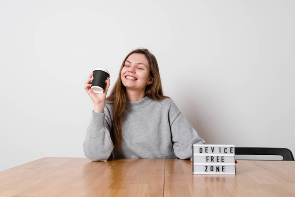 Happy girl sitting relaxed at the table with sign device free zone. Digital detox concept - Φωτογραφία, εικόνα