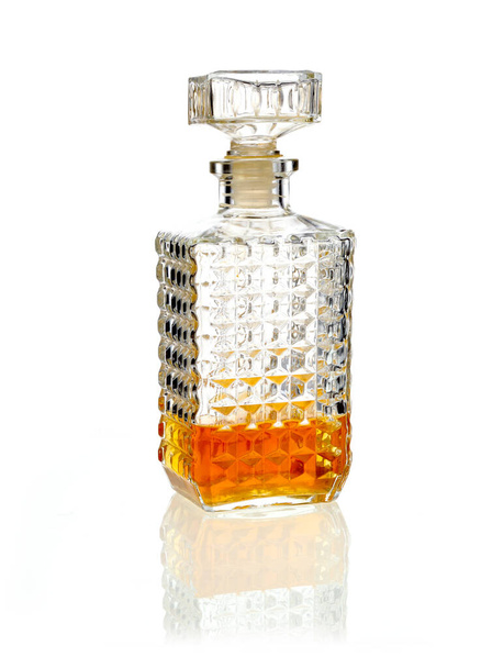 Stoppered whiskey or brandy decanter one third full of alcohol on a reflective white surface - Φωτογραφία, εικόνα