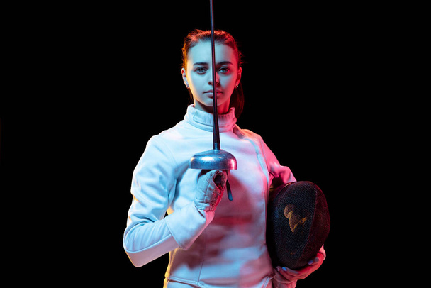 Teen girl in fencing costume with sword in hand isolated on black background - Foto, Bild