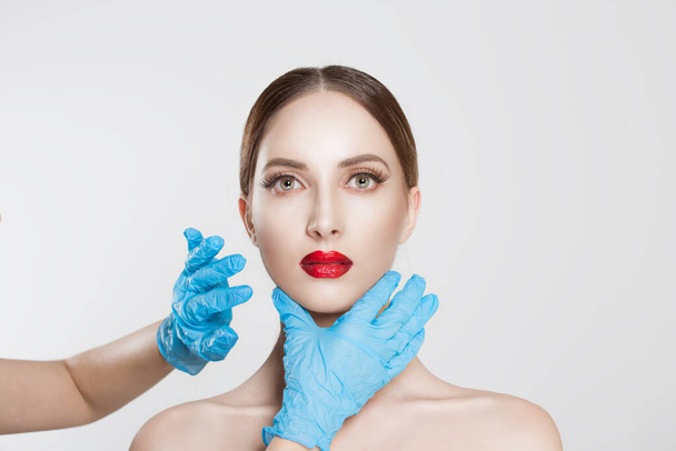 wish to be beautiful need for beauty. Closeup portrait doctor hands with gloves touching woman face chin lips chin want to change her form do plastic surgery. Lips augmentation chin reduction concept - Photo, Image