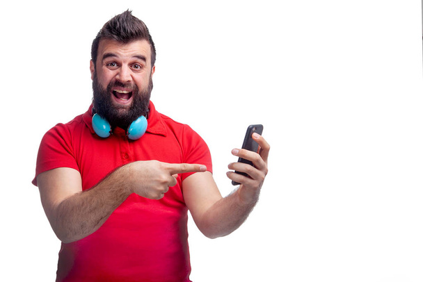 un hombre en una camiseta roja con barba y auriculares sostiene un teléfono en sus manos. - Foto, imagen