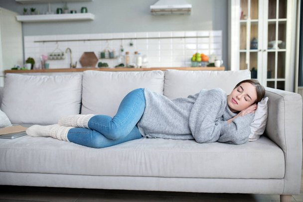 Young girl in a grey sweater having a nap on a sofa - Fotoğraf, Görsel