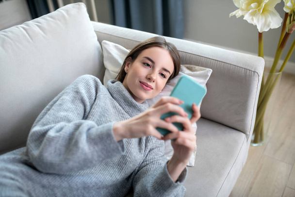 Young girl in a grey sweater holding a smartphone - Photo, Image