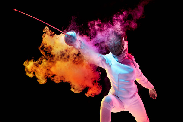 Teen girl in fencing costume with sword in hand isolated on black background - Photo, Image