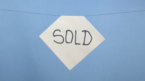 brennendes und rauchendes weißes Blatt Papier mit schwarzer Aufschrift "verkauft" auf blauem Hintergrund - Filmmaterial, Video