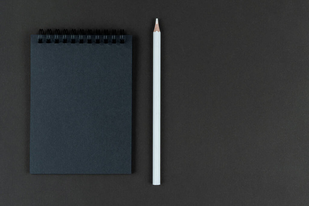 black notebook and white pencil on black background. Mock Up Notepad of black paper and white pencil lying on paper background. Copy space. - Fotografie, Obrázek