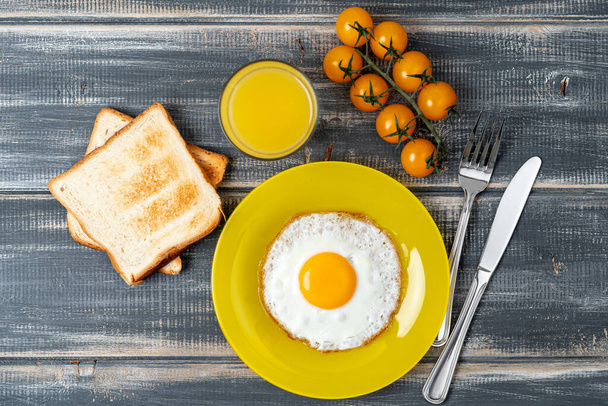 Jajko smażone na żółtym talerzu z pomidorami wiśniowymi, sokiem pomarańczowym i tostem. Smaczne śniadanie.. - Zdjęcie, obraz