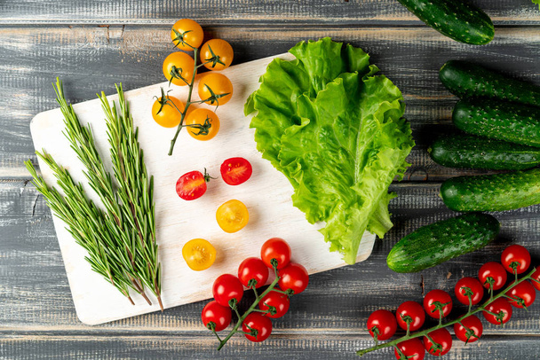 romero, hojas de lechuga, pepinos y tomates de cerezo de rama en tablero de corte blanco. verduras listas para la ensalada - Foto, imagen