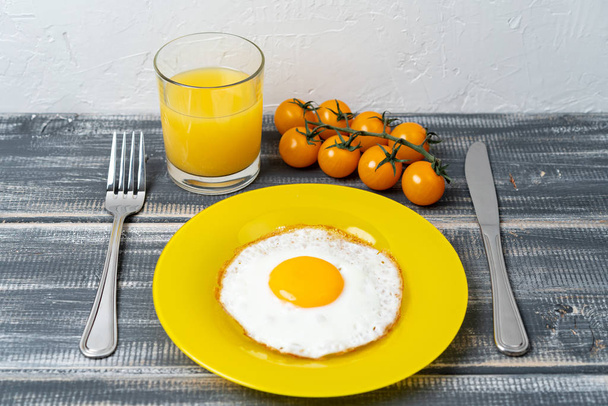 fried egg on yellow plate with cherry tomatoes and orange juice. Light breakfast. - Foto, afbeelding