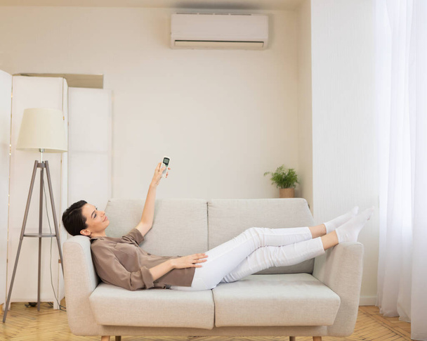 Jonge vrouw schakelen airconditioning in haar huis - Foto, afbeelding