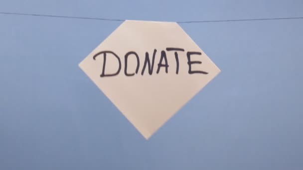 Un hombre cuelga una hoja blanca de papel con una inscripción negra "donar" sobre un fondo azul
 - Metraje, vídeo