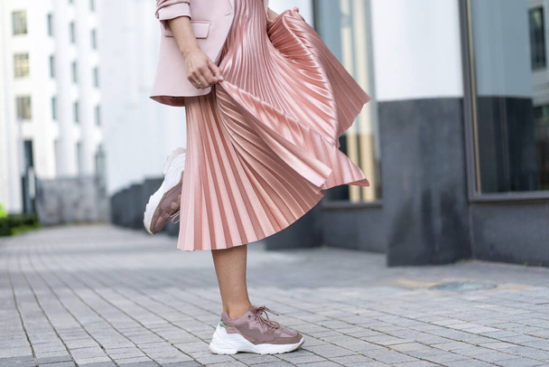 Pleated skirt coral color and sneakers. The girl is very dynamic posing on the street, the skirt is developing. - Foto, Bild