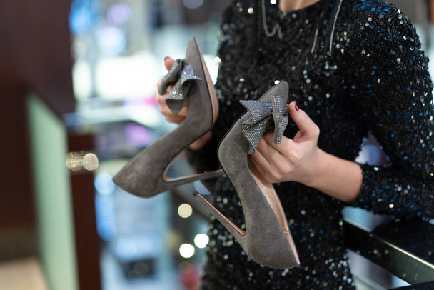 Womens gray suede shoes with high heels with a decorative bow element with rhinestones on heels. Close-up in hands of a model on a blurred natural background - Fotografie, Obrázek