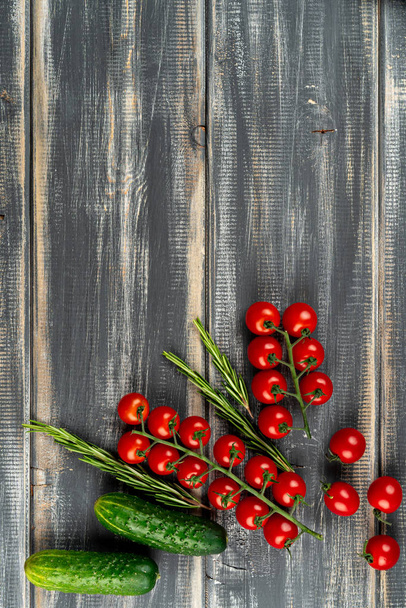 Zweig Kirschtomaten, Gurken und Rosmarin auf schwarzem Holztisch. Kopierraum - Foto, Bild