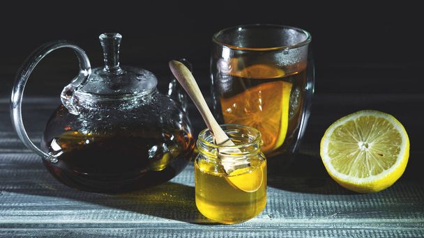 honey, lemon and black tea in thermostat on black wooden table. Tea ceremony  - Photo, Image