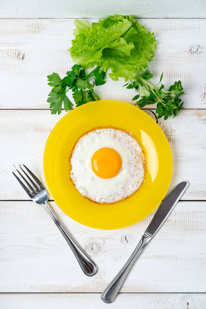 fried egg on yellow plate with lettuce and fragrant greens. Light breakfast. - Fotoğraf, Görsel