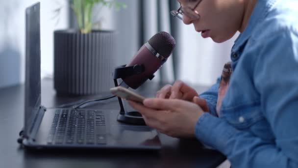 Portrait of young female blogger conducting a live stream, speaks into a micraphon. woman leads podcast at home in front of laptop - Materiał filmowy, wideo