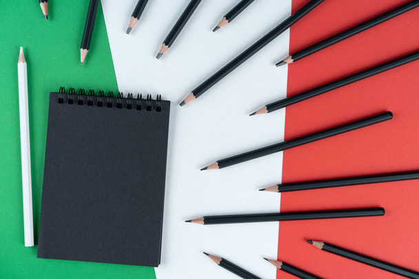 Blacklist Italy. black notebook, many black pencils and one white pencil lies on Italian flag. Mock up, copy space, pattern, cardboard texture. - Foto, Imagen