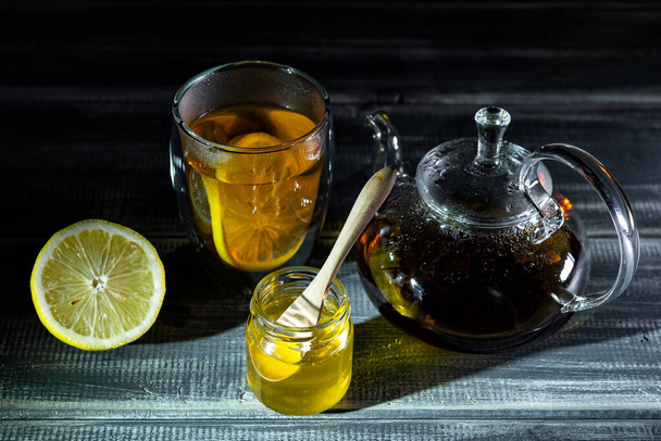 med, citron a černý čaj v termostatu na černém dřevěném stole. Čajový obřad  - Fotografie, Obrázek